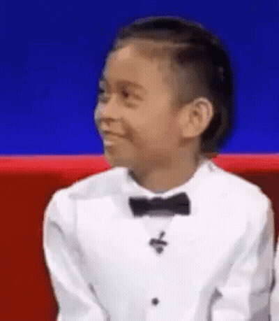 A Young Boy Is Wearing A Tuxedo And Bow Tie And Smiling . GIF