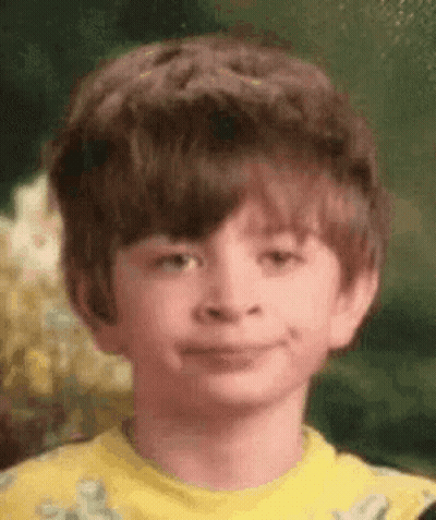 A Young Boy Is Wearing A Yellow Shirt And Smiling . GIF
