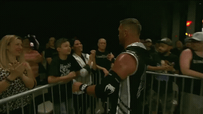 A Young Boy Kisses A Man On The Cheek In Front Of A Crowd GIF