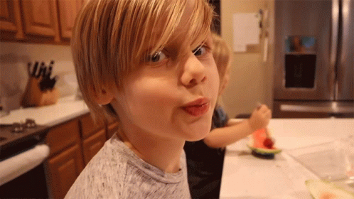 A Young Boy Making A Funny Face With His Tongue Out In Front Of A Refrigerator GIF