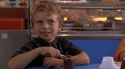A Young Boy Sits At A Table With A Cup Of Chocolate Pudding GIF