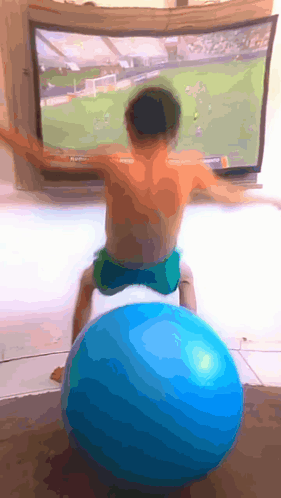 A Young Boy Sits On A Blue Exercise Ball In Front Of A Tv GIF