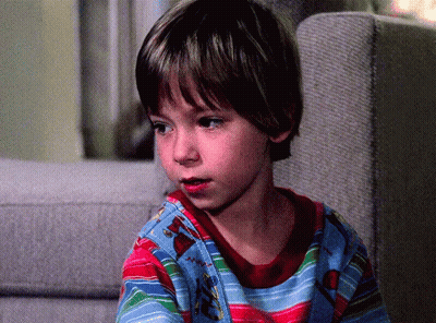 A Young Boy Sitting On A Couch Wearing A Striped Shirt With A Christmas Tree On It GIF