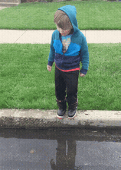 A Young Boy Standing In A Puddle With His Reflection In The Puddle GIF