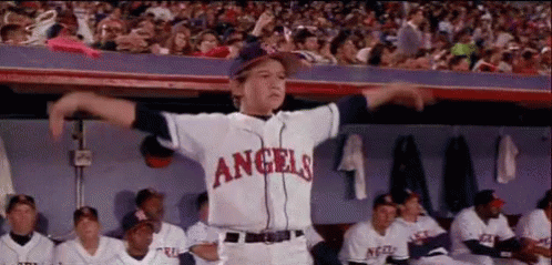 A Young Boy Wearing A Angels Baseball Uniform Is Standing In The Dugout With His Arms Outstretched . GIF