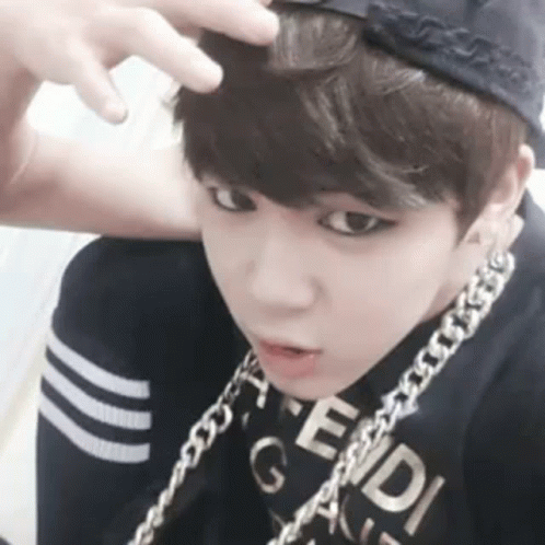 A Young Boy Wearing A Baseball Cap And A Chain Around His Neck Is Looking At The Camera . GIF