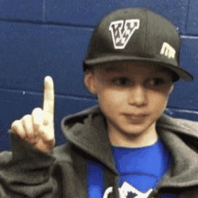 A Young Boy Wearing A Baseball Cap With The Letter V On It Is Giving The Middle Finger . GIF