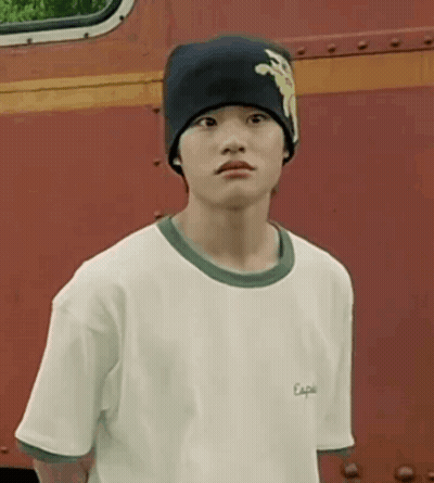 A Young Boy Wearing A Beanie And A White T-Shirt Is Standing In Front Of A Red Truck . GIF