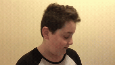 A Young Boy Wearing A Black And Gray Shirt Is Making A Funny Face GIF