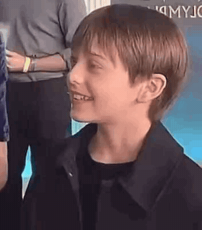 A Young Boy Wearing A Black Jacket Is Smiling And Looking At The Camera . GIF