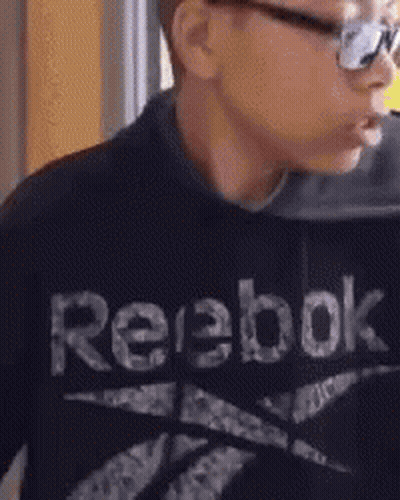 A Young Boy Wearing A Black Reebok Sweatshirt Is Eating Something . GIF
