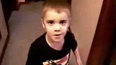 A Young Boy Wearing A Black Shirt Is Standing In A Hallway . GIF