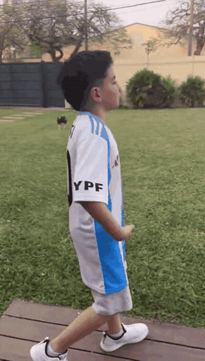 A Young Boy Wearing A Blue And White Ypf Jersey Walks Across A Wooden Deck GIF