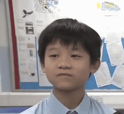 A Young Boy Wearing A Blue Shirt And Tie Is Sitting In Front Of A Bulletin Board . GIF
