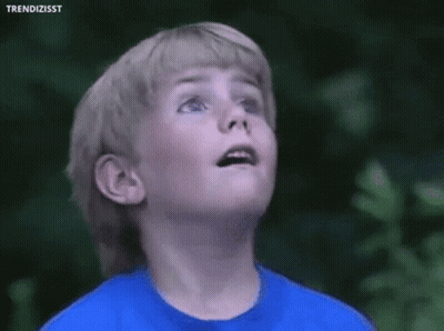 A Young Boy Wearing A Blue Shirt Is Looking Up At The Sky . GIF