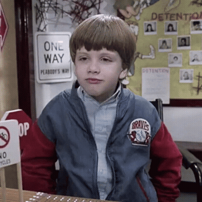 A Young Boy Wearing A Braves Jacket Is Sitting At A Desk In Front Of A One Way Sign . GIF