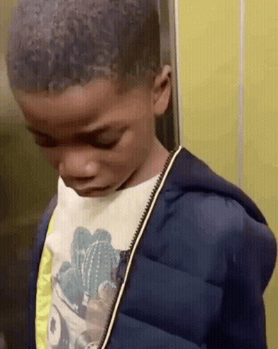 A Young Boy Wearing A Cactus Shirt And A Blue Jacket Is Standing In An Elevator Looking Down . GIF