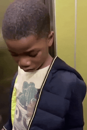 A Young Boy Wearing A Cactus Shirt And A Blue Jacket Looks Down GIF