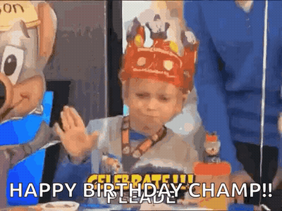 A Young Boy Wearing A Crown Is Sitting At A Table With A Chuck E Cheese Mascot . GIF
