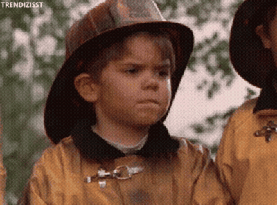 A Young Boy Wearing A Fireman 'S Hat And A Yellow Jacket GIF