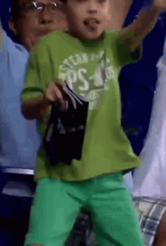 A Young Boy Wearing A Green Shirt And Green Shorts Is Dancing In A Crowd . GIF