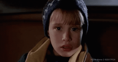 a young boy wearing a hat and scarf is looking at the camera with a surprised look on his face .