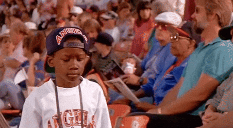 A Young Boy Wearing A Hat With The Word Angels On It Is Sitting In A Crowd Of People At A Baseball Game . GIF