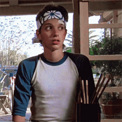 A Young Boy Wearing A Headband And A Baseball Shirt Is Holding Chopsticks GIF