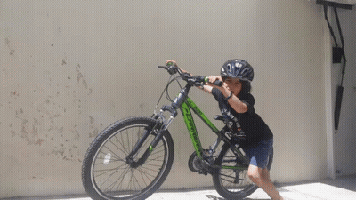 A Young Boy Wearing A Helmet Is Standing Next To A Green Bicycle GIF