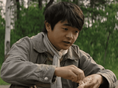 A Young Boy Wearing A Jacket And Scarf Is Eating A Piece Of Food GIF