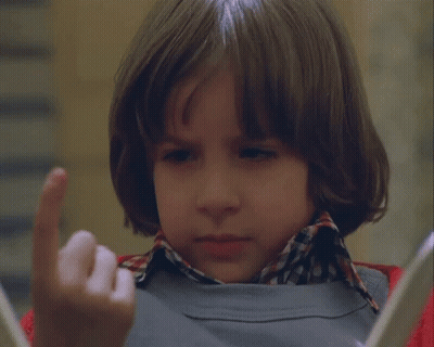 A Young Boy Wearing A Plaid Shirt And A Grey Sweater Looks At Something GIF