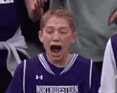 A Young Boy Wearing A Purple Basketball Jersey Is Screaming While Watching A Game . GIF