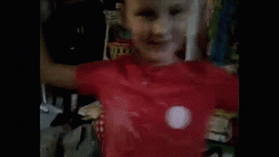 A Young Boy Wearing A Red Shirt Is Standing In Front Of A Shelf GIF