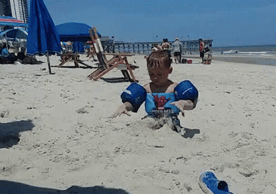 A Young Boy Wearing A Spiderman Shirt Is Playing In The Sand On The Beach GIF