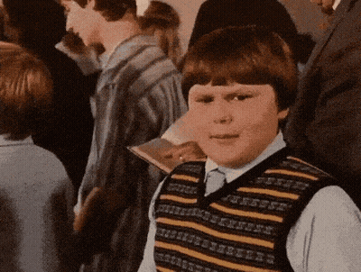 A Young Boy Wearing A Striped Vest Stands In A Crowd Of People GIF