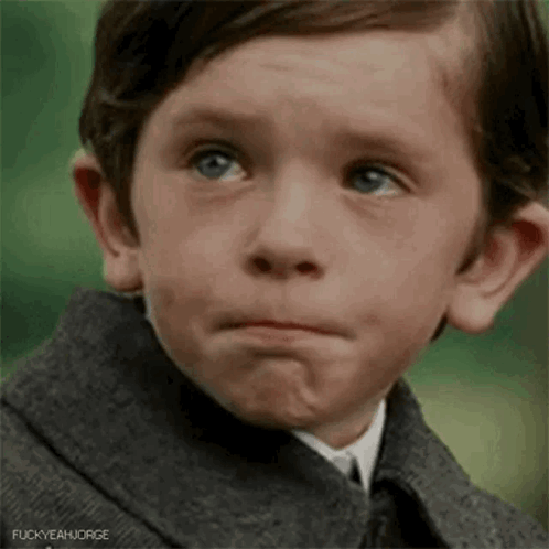 A Young Boy Wearing A Suit And Tie Is Making A Sad Face . GIF