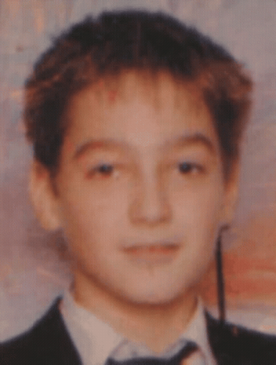 A Young Boy Wearing A Suit And Tie Looks At The Camera GIF