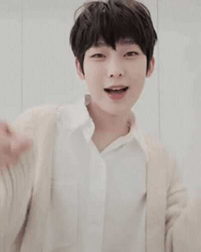 A Young Boy Wearing A White Shirt And A Beige Cardigan Is Smiling And Pointing . GIF