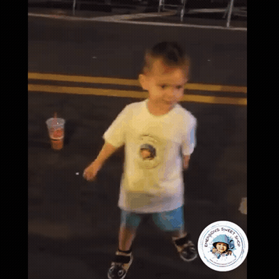 A Young Boy Wearing A White Shirt With A Picture Of A Man On It Is Walking Down A Street GIF