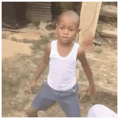 A Young Boy Wearing A White Tank Top And Blue Shorts Is Standing In A Dirt Field . GIF