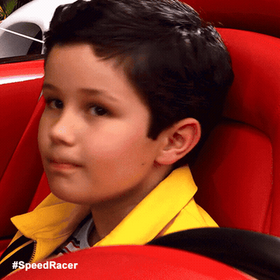 A Young Boy Wearing A Yellow Jacket Is Sitting In A Red Car With The Hashtag #Speedracer GIF