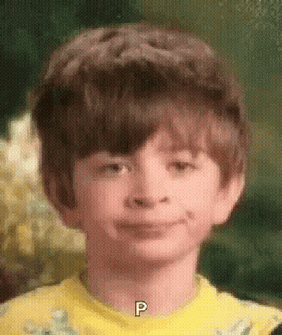 A Young Boy Wearing A Yellow Shirt Is Smiling And Has The Letter P On His Neck . GIF