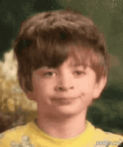 A Young Boy Wearing A Yellow Shirt Is Smiling For The Camera . GIF
