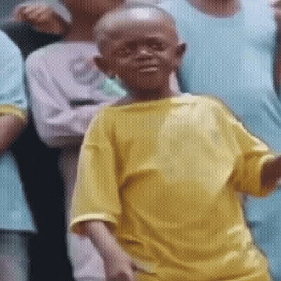A Young Boy Wearing A Yellow Shirt Is Standing In Front Of A Group Of People . GIF