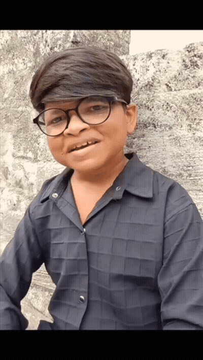 A Young Boy Wearing Glasses And A Black Shirt Is Smiling For The Camera GIF
