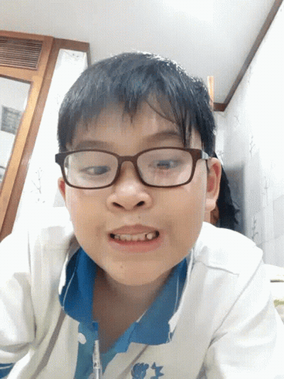 A Young Boy Wearing Glasses And A Blue Shirt Is Smiling For The Camera GIF