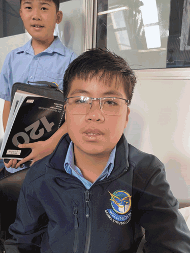 A Young Boy Wearing Glasses And A Jacket That Says Wellington On It GIF