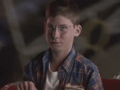 A Young Boy Wearing Glasses And A Plaid Shirt Is Sitting In A Chair And Making A Funny Face . GIF