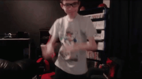 A Young Boy Wearing Glasses And A White Shirt Is Dancing In A Dark Room . GIF