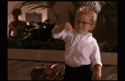 A Young Boy Wearing Glasses And A White Shirt Is Standing Next To A Suitcase And Giving A Thumbs Up . GIF